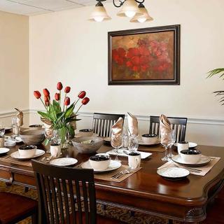 A beautifully arranged dining room with a large wooden table, set for a meal with elegant dinnerware and a centerpiece of flowers.