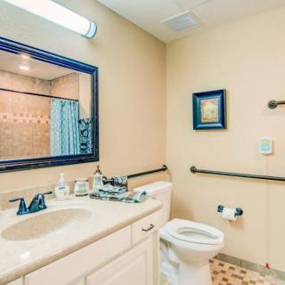 A well-lit bathroom featuring a sink, mirror, toilet, and bathtub with a patterned tile floor.