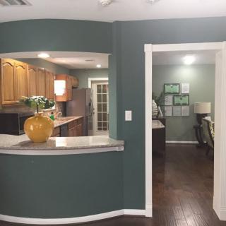 A home interior featuring an open layout with a kitchen and living area, highlighted by dark wood floors and green walls.