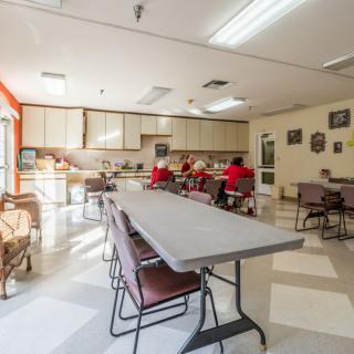 A community dining area with tables, chairs, and a kitchen in the background.