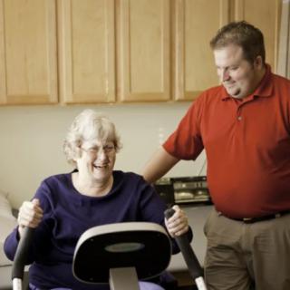 An elderly woman exercising with assistance from a caregiver or trainer.