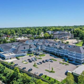 Aerial view of a modern building complex with a parking lot surrounded by trees on a sunny day.