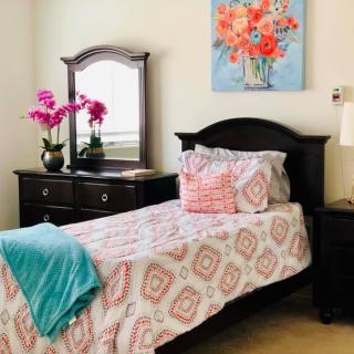 A cozy bedroom with a single bed adorned with patterned bedding, a dresser with a mirror, and colorful floral accents.