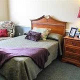 A cozy bedroom with a bed, nightstand, and upholstered chair.