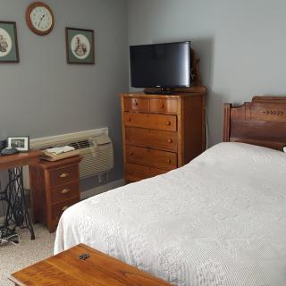 A cozy bedroom featuring vintage-style wooden furniture, including a bed and dresser, with a TV on top.