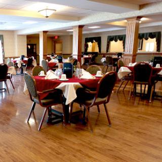 A spacious and elegantly arranged dining area featuring tables with red tablecloths and wooden flooring.