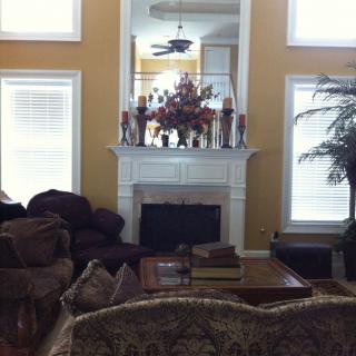 A cozy living room with a fireplace, surrounded by sofas and a coffee table, adorned with decorative items and large windows.