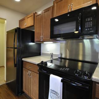 A modern kitchen with stainless steel appliances, wooden cabinets, and a black countertop.