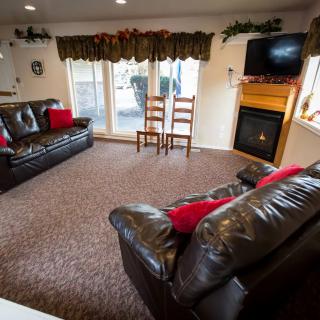 A cozy living room featuring leather sofas, a television above a fireplace, and large windows with drapes.