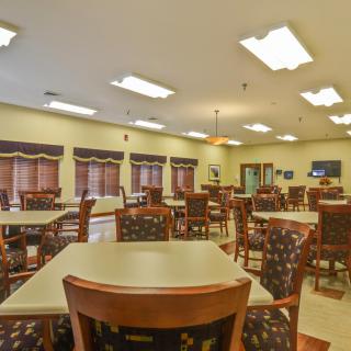 An empty dining hall with neatly arranged tables and chairs, illuminated by overhead lighting.