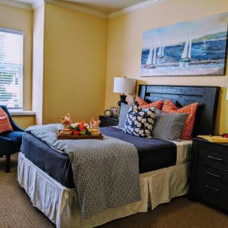A cozy bedroom with a neatly made bed, decorative cushions, and nautical-themed artwork above the headboard.