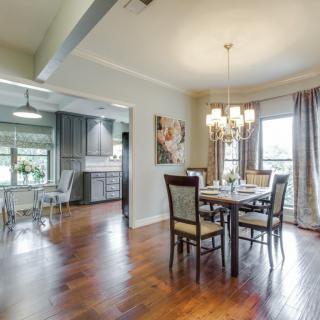A modern dining area with hardwood flooring and a chandelier, adjoining a kitchen with ample natural light.