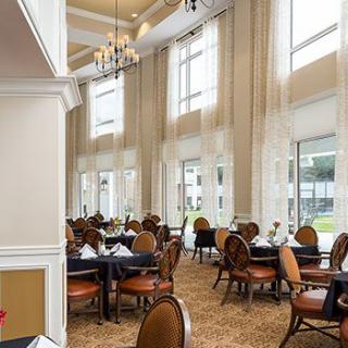 An elegant dining area with large windows and chandeliers, featuring neatly arranged empty tables.