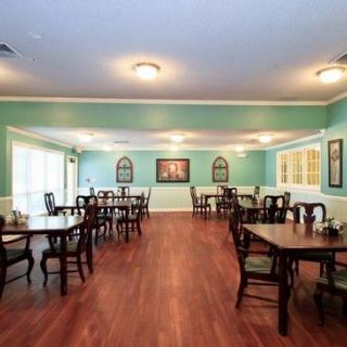 A well-arranged dining room with wooden floors and neatly set tables and chairs, illuminated by ceiling lights.