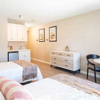 A modern hotel room with twin beds, a small kitchenette, and a seating area.