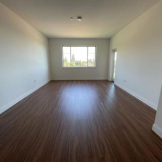 An empty room with wooden flooring and a large window allowing natural light in.
