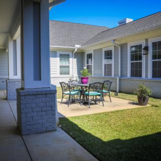 A cozy outdoor patio area with a round table and chairs, surrounded by a well-maintained lawn in a courtyard setting.
