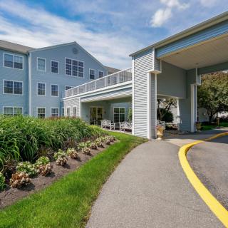 A modern building with a landscaped entrance and driveway under a clear blue sky.
