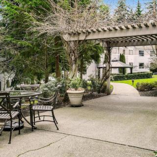 A peaceful garden patio with a pergola, surrounded by lush greenery and outdoor seating.