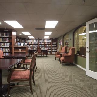 A quiet library room with bookshelves, tables, and chairs for reading and study.