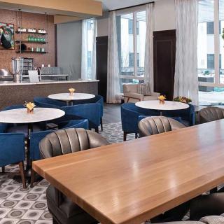 A modern and stylish cafe interior with a mix of round and rectangular tables, comfortable seating, and a coffee bar backdrop.