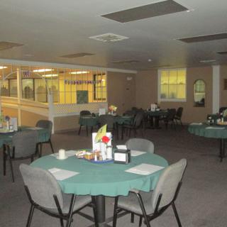 A spacious dining area with multiple tables and chairs neatly arranged, featuring green tablecloths under soft indoor lighting.