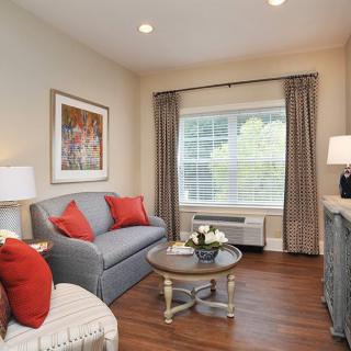 A cozy living room with a gray sofa, red cushions, and a coffee table set in front of a large window.
