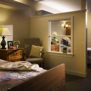 A cozy bedroom interior with a comfortable chair, wooden furniture, and a lamp by the window.