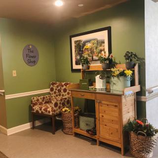 A cozy corner with green walls, featuring a patterned chair, a wooden table adorned with flowers and decorative items, and a picture on the wall.