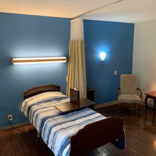 A well-lit hospital room featuring a single bed with striped bedding, accompanied by a chair and side table.
