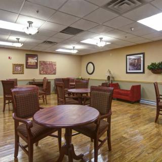 A cozy lounge area with wooden tables and chairs on a polished wood floor, featuring framed artwork and comfortable seating.