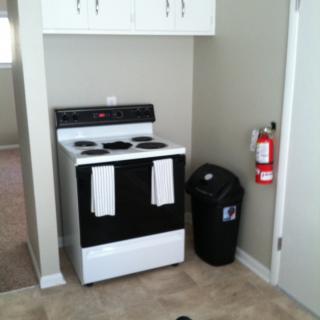 A kitchen area featuring a stove with towels, a garbage can, and a fire extinguisher.