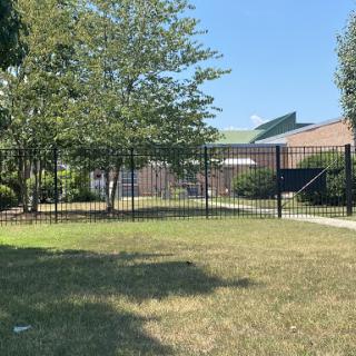 A fenced area with well-maintained grass and trees under a clear blue sky.