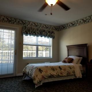 A cozy bedroom with a single bed, ceiling fan, and floral wallpaper.