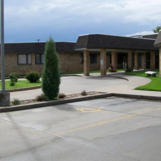 A small building with a parking lot and landscaped greenery in front under a cloudy sky.