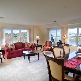 A spacious living and dining area with elegant furniture and large windows overlooking a lake.
