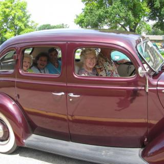 A group of people sitting inside a vintage maroon car parked outdoors.