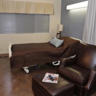 A hospital room featuring a bed, a reclining chair, and a small table with a lamp.
