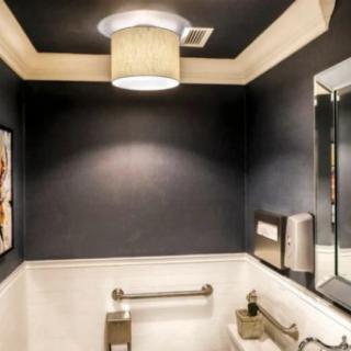 A modern and minimalist bathroom with dark walls, featuring a stylish lighting fixture and decorative wall art.