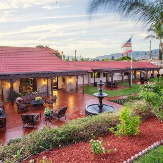 A spacious outdoor patio area with seating arrangements, a fountain, and well-maintained gardens under a clear sky.