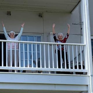 Two joyful individuals wave from their balcony, celebrating together.