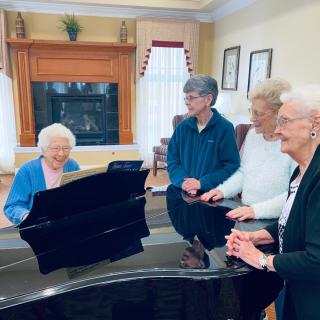A group of elderly individuals enjoying a musical moment around a piano.