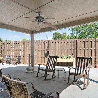 A shaded patio area with outdoor seating and a ceiling fan, enclosed by a wooden fence.