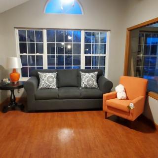 A cozy living room with a gray sofa, an orange armchair, and large windows.