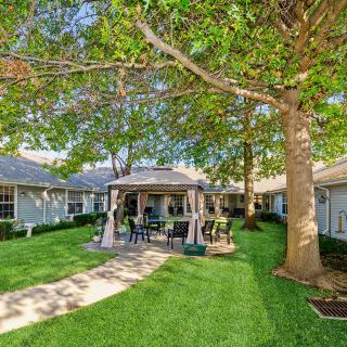A peaceful backyard with a gazebo, lush lawn, and outdoor furniture surrounded by trees.