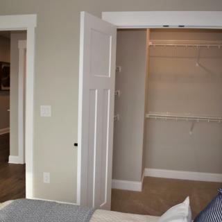 A bedroom interior featuring an open closet with shelving and a partially visible bed.