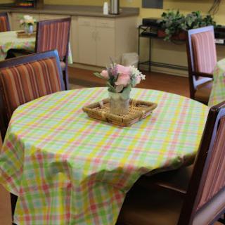 A cozy dining area featuring a round table dressed with a colorful checkered tablecloth and a decorative arrangement of flowers.