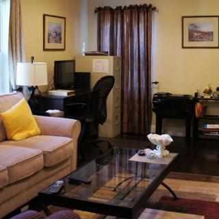 A cozy living room with a home office setup, featuring a sofa, coffee table, and desk with a computer.