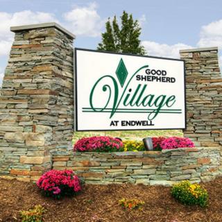 Entrance sign for Good Shepherd Village at Endwell surrounded by flowers and stone pillars.