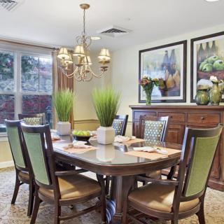A beautifully decorated dining room featuring a wooden table, chairs with green accents, a chandelier, and artwork on the walls.